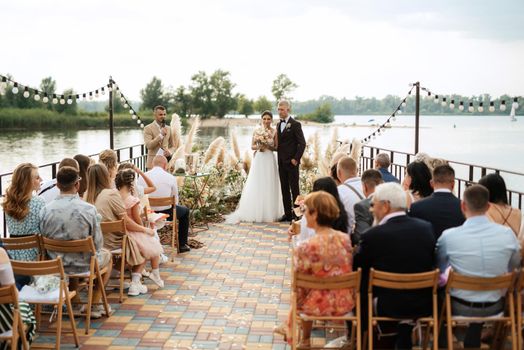 wedding ceremony on a high pier near the river with invited guests