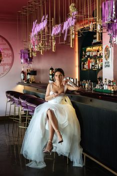 bride inside the cocktail bar at the bar in a bright atmosphere with a glass of drink