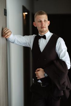 portrait of the groom in a brown three-piece suit with a bow tie on the wedding day