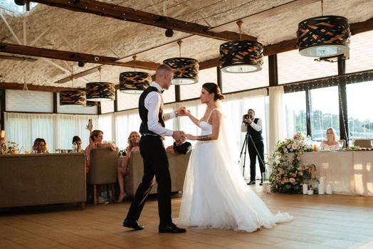 the first wedding dance of the bride and groom inside the restaurant hall in sunset light