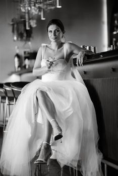 bride inside the cocktail bar at the bar in a bright atmosphere with a glass of drink