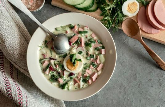 Traditional Russian cold summer soup - okroshka with fresh vegetables, sausage and kefir. Composition with traditional dishes and spices. View from above.