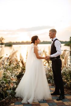 bride and groom against the backdrop of a yellow sunset on a pier near the river