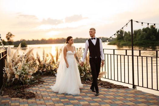 bride and groom against the backdrop of a yellow sunset on a pier near the river