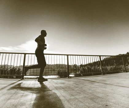 Man is running quickly on the shore bridge. Silhouette of active man exercising and stretching on the lake street. Healthy lifestyle. Alone young fitness man.