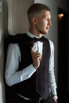 portrait of the groom in a brown three-piece suit with a bow tie on the wedding day