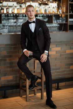 portrait of the groom in a brown three-piece suit with a bow tie on the wedding day