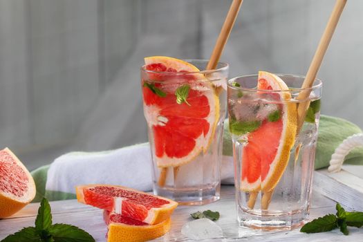 Summer refreshing cocktails with grapefruit slices and mint on a white wooden tray.