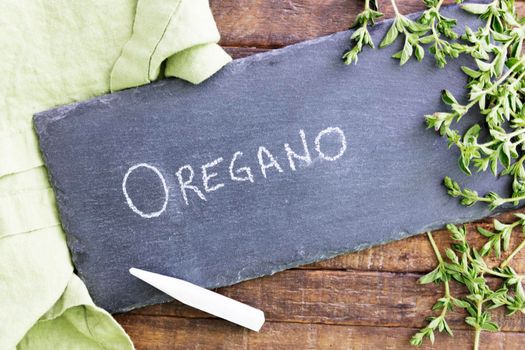 Fresh oregano and a chalkboard sign with oregano wriiten on it.