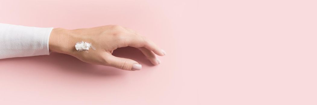 Hand of beautiful young girl with cream on pink pastel background. Concept template feminine blog, social media, beauty concept. Web banner.