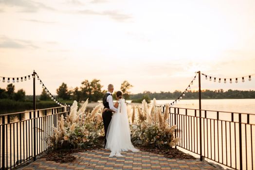 bride and groom against the backdrop of a yellow sunset on a pier near the river