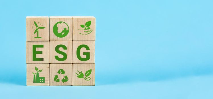 ESG Words on a wood cubes. ESG concept of environmental, social and governance. Wooden cube with abbreviation ESG standing with other icons on blue background.