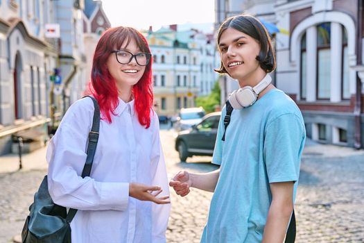 Portrait of teenage young guy and girl students looking at camera, outdoor. Couple of young people with backpacks, on city street. Teenagers, lifestyle, urban style, joy, friendship, education concept