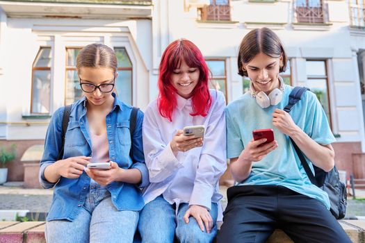 Teenage friends together outdoor having fun using smartphones on city street. Technology mobile apps, lifestyle, vacation leisure, urban style, youth concept