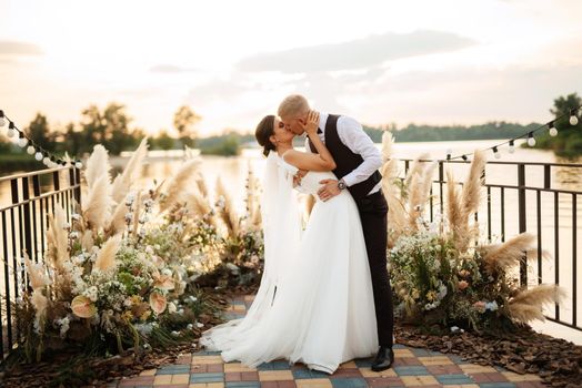 bride and groom against the backdrop of a yellow sunset on a pier near the river