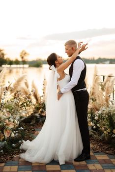 bride and groom against the backdrop of a yellow sunset on a pier near the river