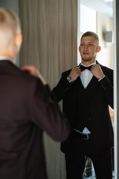 portrait of the groom in a brown three-piece suit with a bow tie on the wedding day