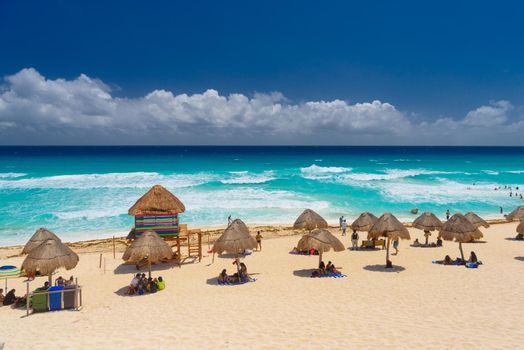 Umbrelas on a sandy beach with azure water on a sunny day near Cancun, Mexico.