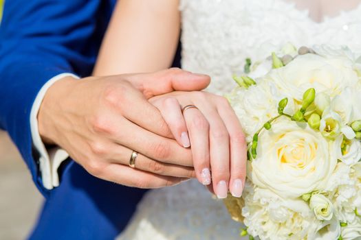 The couple cuddling and holding bridal bouquet. Hands close-up.