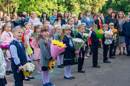 NOVOKUZNETSK, KEMEROVO REGION, RUSSIA - SEP, 1, 2021: Meeting with the first-grade pupils and teacher at schoolyard. The day of knowledge in Russia.