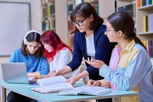 Group of teenage students study in school library classroom. Teen girl and female teacher mentor helping in their studies. High school, learning, education, knowledge, adolescence