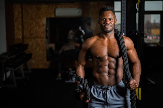 Muscular african american man posing with rope in gym