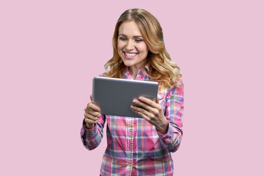 Young happy woman talking via internet on color background. Pretty caucasian girl using digital tablet on pink background.