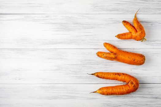 Top view close-up of several ripe orange ugly carrots lie on a light wooden surface with copy space for text. Selective focus.