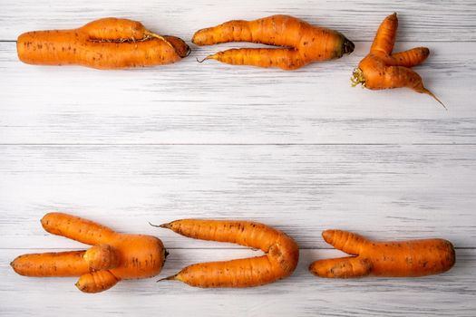 Top view close-up of several ripe orange ugly carrots lie on a light wooden surface with copy space for text. Selective focus.