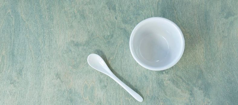 banner with empty white cup with white spoon on green wooden background. Copy space. Top view