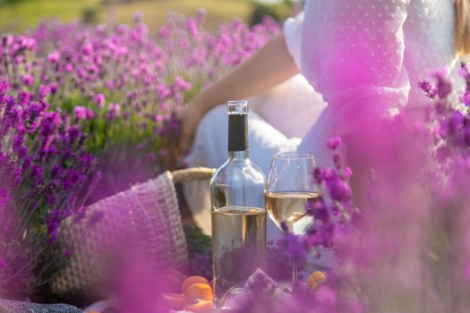 The girl is resting in a lavender field, drinking wine. Selective focus. Relaxation