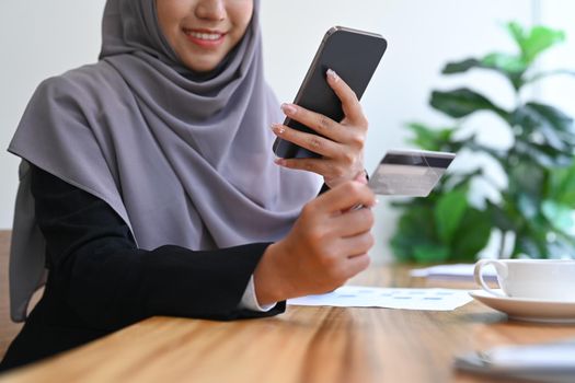 Young Muslim woman in hijab holding credit card and using mobile phone. Online shopping, internet banking concept.