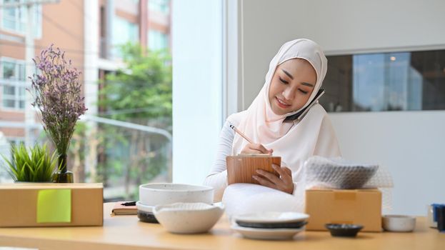 Asian young Muslim woman confirming orders from customer on cellphone. E-commerce, Online selling concept.