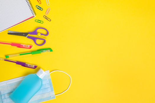 protective mask, disinfectant gel and school supplies on yellow background, concept of new normality for children and protection against viruses, copy space for text