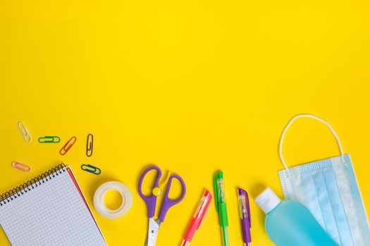 protective mask, disinfectant gel and school supplies on yellow background, concept of new normality for children and protection against viruses, copy space for text