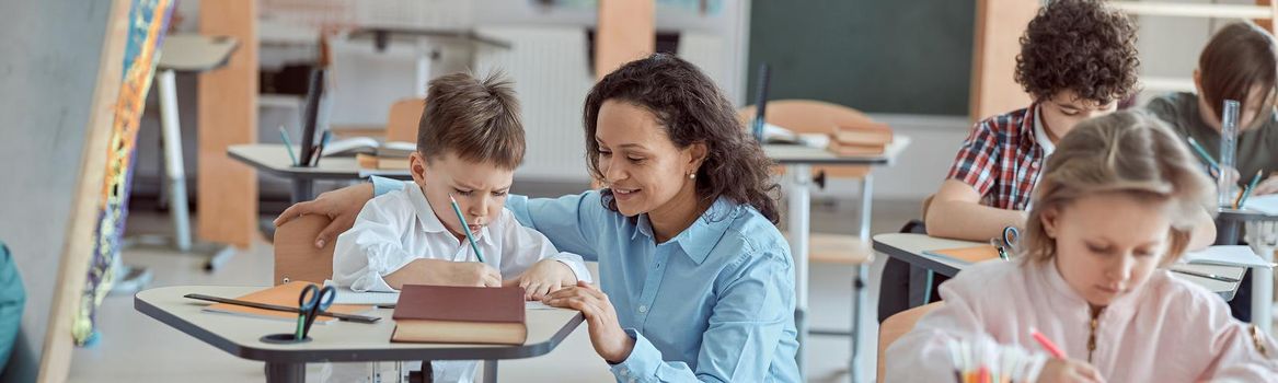 Happy kind teacher is helping kids in elementary school lessons.