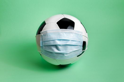 soccer ball with protective mask on green background, concept of new normality in sports