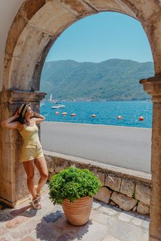 Summer photo shoot on the streets of Kotor, Montenegro. Beautiful girl in white dress and hat. smiling tourist girl with hat. Spectacular view of Montenegro with copy space. fashion outdoor photo of beautiful sensual woman with blond hair in elegant dress and straw hat and bag, posing in Montenego's city Perast