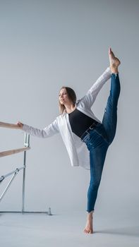 Caucasian woman in casual clothes pulls the longitudinal split at the ballet barre