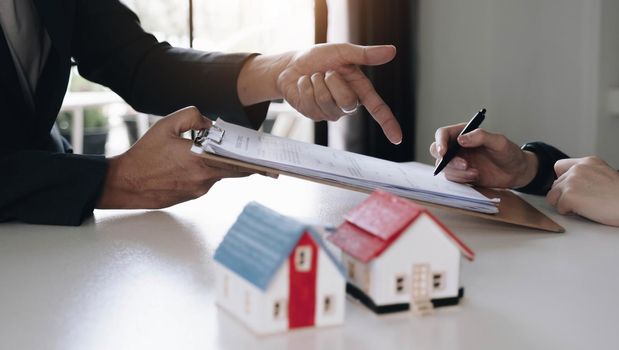 Real estate agent with house model hand putting signing contract,have a contract in place to protect it,signing of modest agreements form in office.Concept real estate,moving home or renting property.