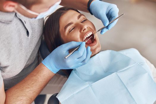 Confident mature doctor is checking teeth of young beautiful happy caucasian woman in modern clinic