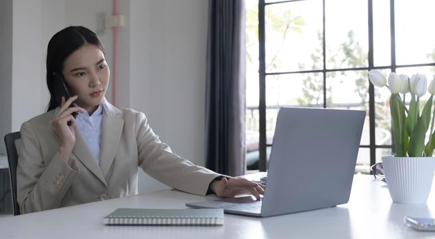 Asian businesswoman talking on a cell phone with a serious expression while working in the office.