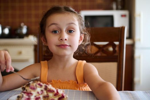 Adorable European kid, little girl looking at camera while enjoying delicious homemade sweet summer dessert, cherry pie, monastery log made from pastry sticks filled with cherry berries. Confectionery