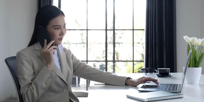 Asian businesswoman talking on a cell phone with a serious expression while working in the office.