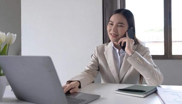 Young Asian woman talking on the phone using a laptop computer in the office..