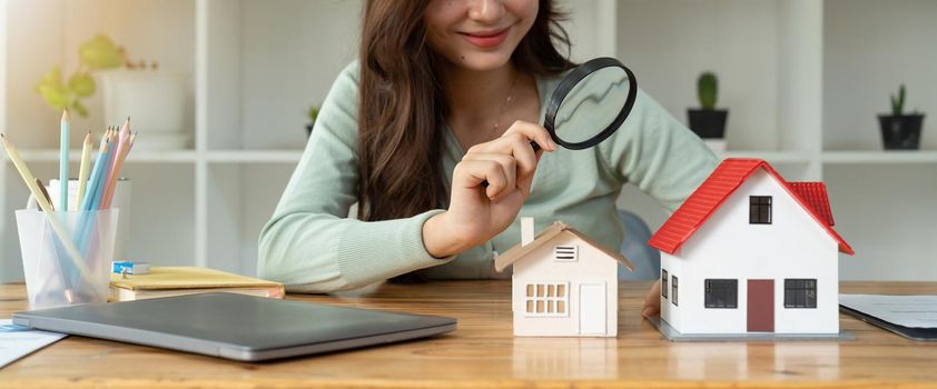 Looking for real estate agency, property insurance, mortgage loan or new house. Woman with magnifying glass over a wooden house at her office.