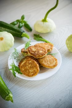 fried vegetable pancakes from squash and zucchini with herbs, on a light wooden table.