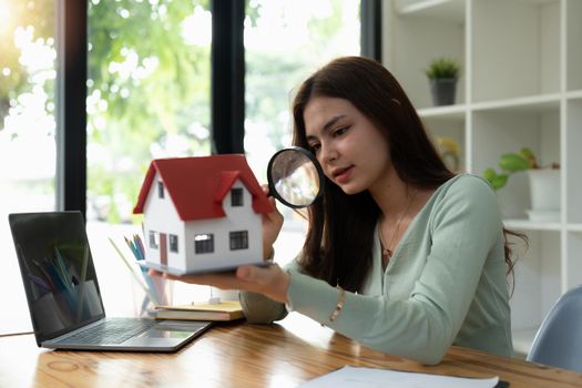 Looking for real estate agency, property insurance, mortgage loan or new house. Woman with magnifying glass over a wooden house at her office.