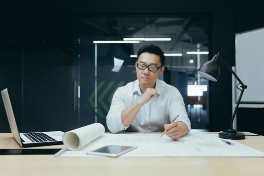 Thinking asian engineer architect working in modern design office, man looking at drawing plan.