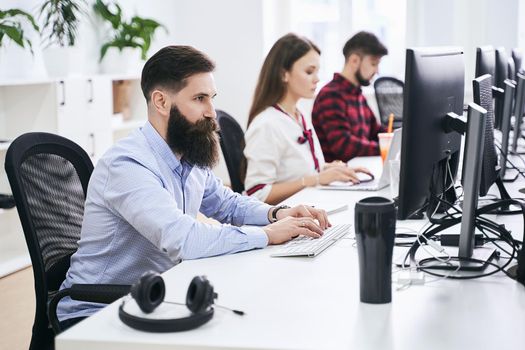 People working in modern IT office. Group of young programmers and software developers sitting at desks working on computers. Team at work.